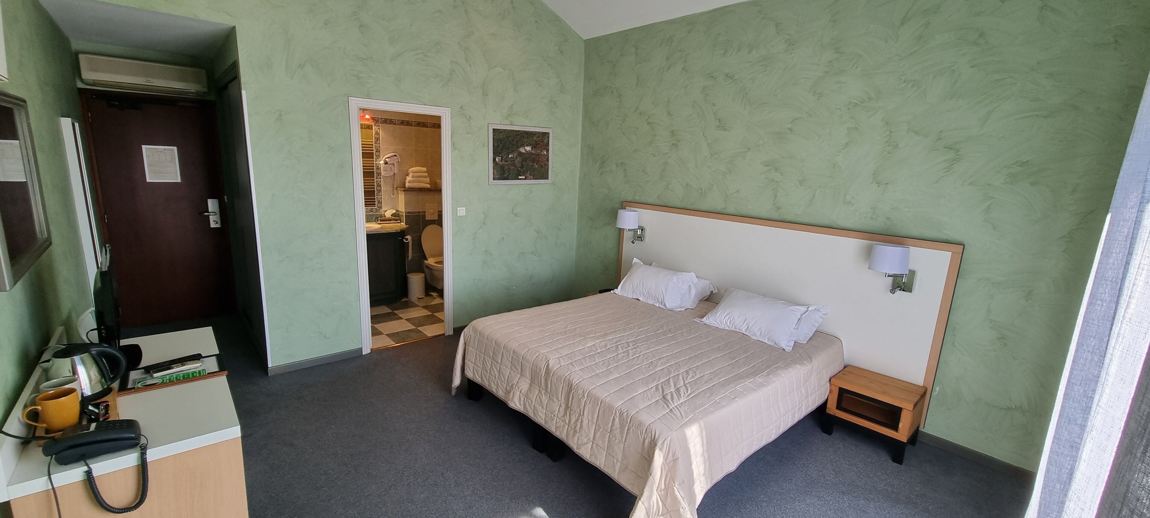 A hotel room with a bed, bedside lamps, a desk with a telephone, and a small table.