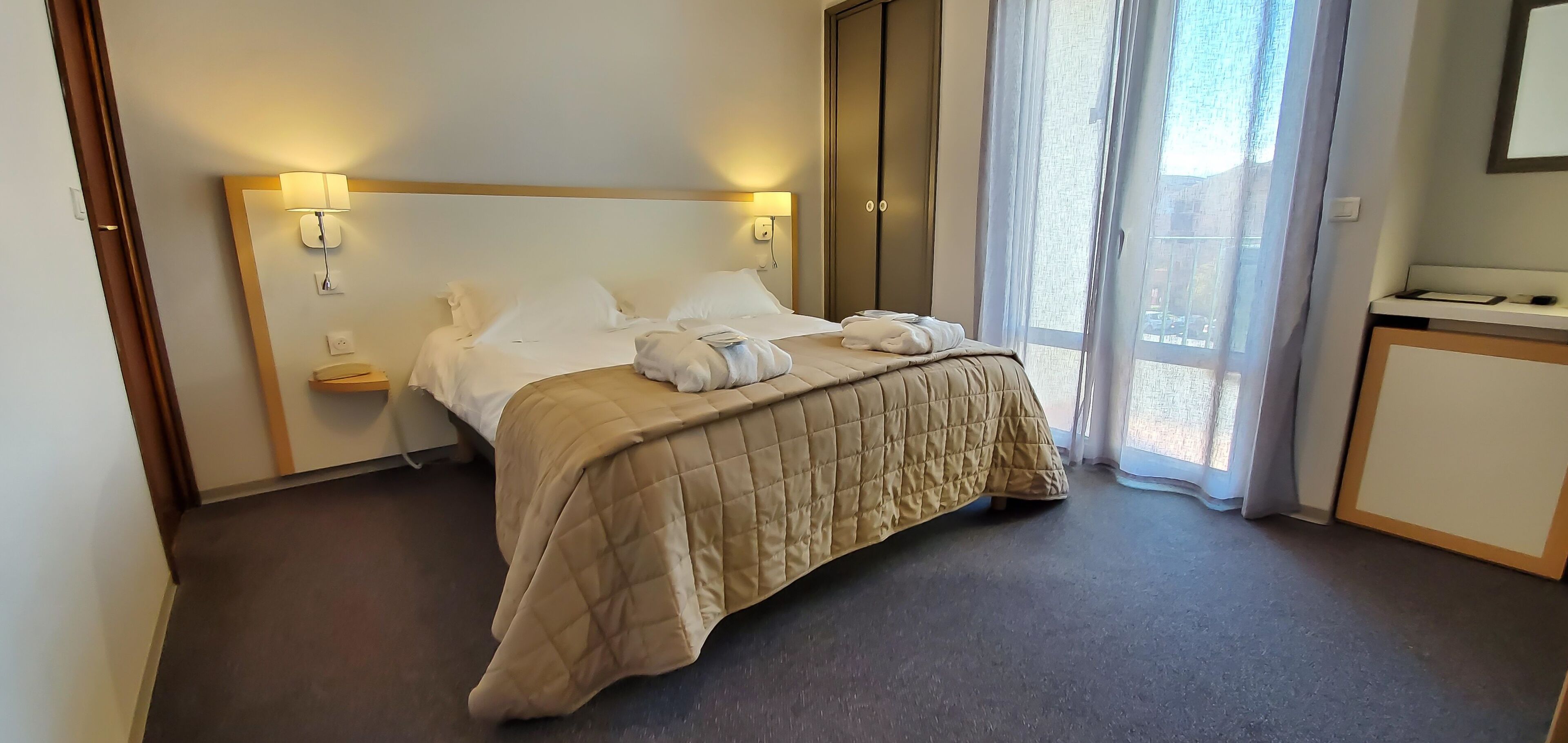 A hotel room with a bed, bedside lamps, a wardrobe, and a desk.