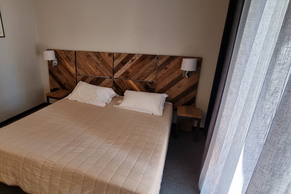 Una habitación de hotel con una cama grande, cabecero de madera, dos lámparas de noche y un cuadro enmarcado en la pared.