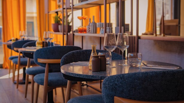 L'intérieur d'un restaurant avec des tables rondes, des chaises bleues et des verres à vin.