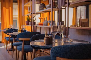 L'intérieur d'un restaurant avec des tables rondes, des chaises bleues et des verres à vin.