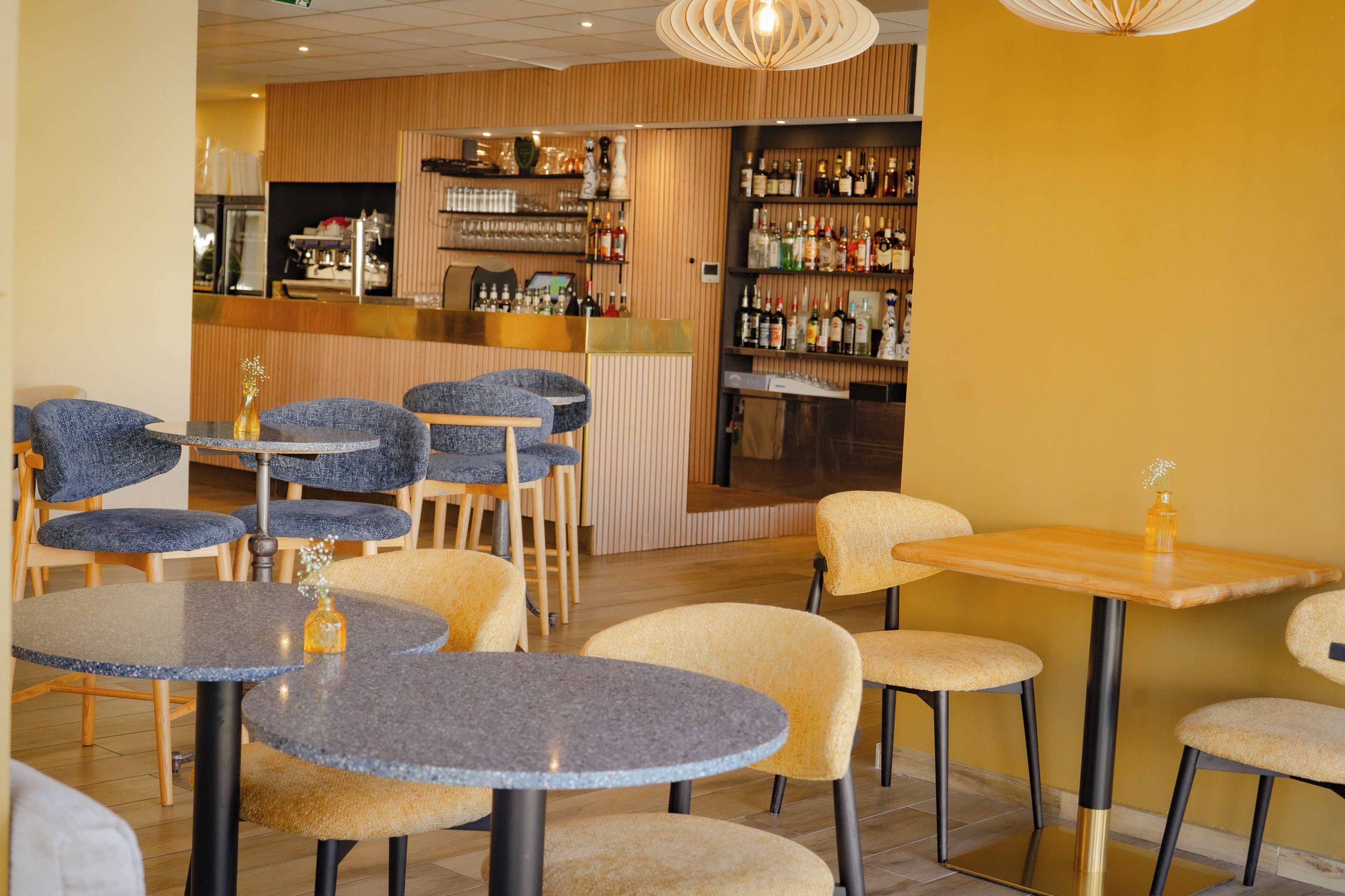 A restaurant with round tables, chairs, and a bar area with shelves of bottles.