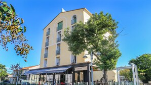 Un hôtel doté d’un espace extérieur couvert avec des sièges, d’une enseigne indiquant un restaurant et d’un arbre devant l’entrée.