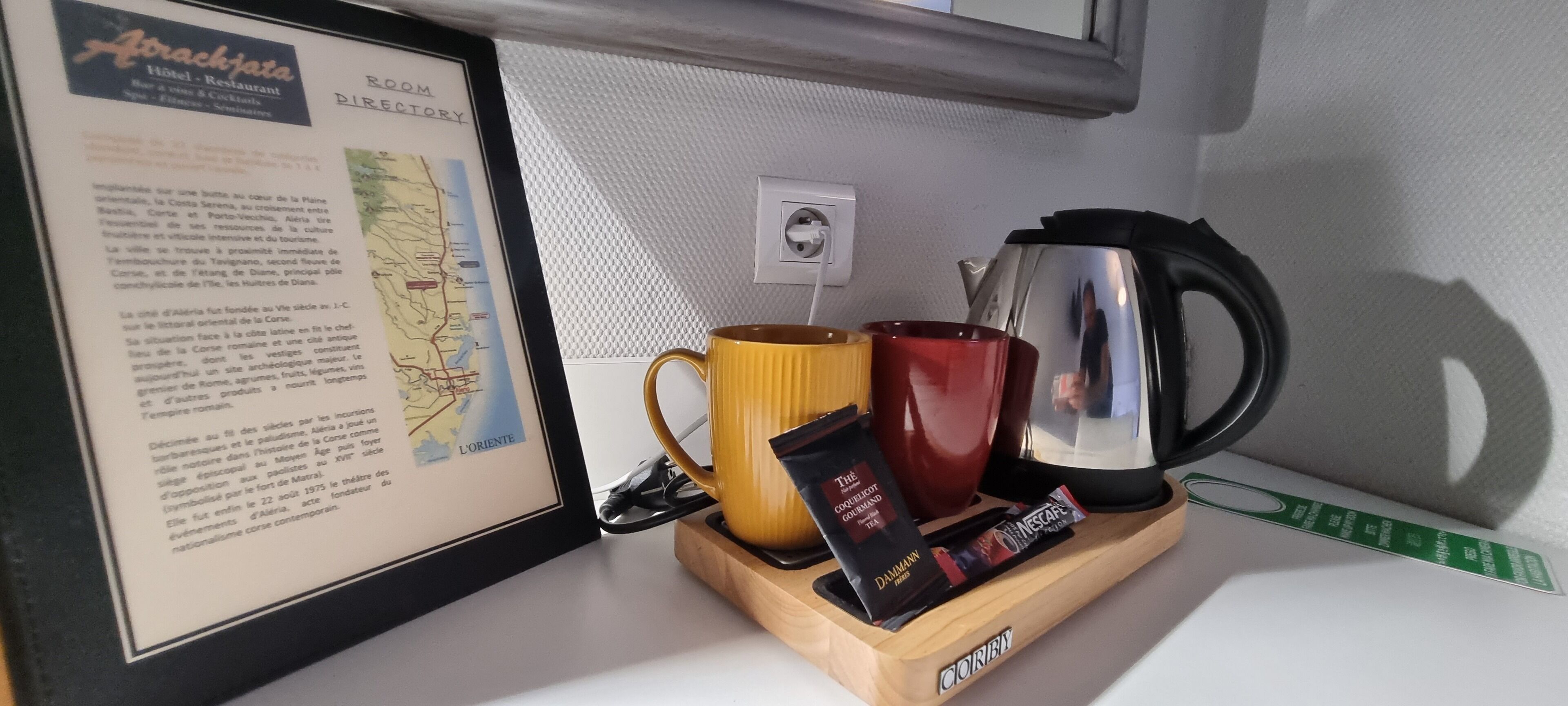 A framed informational poster, a coffee maker, two mugs, and a tea packet on a wooden tray.