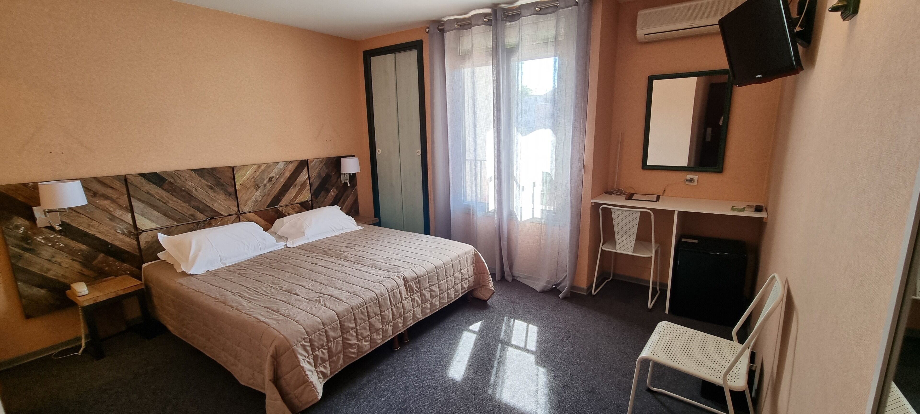 A hotel room with a bed, a desk, a chair, a TV, and a mirror.