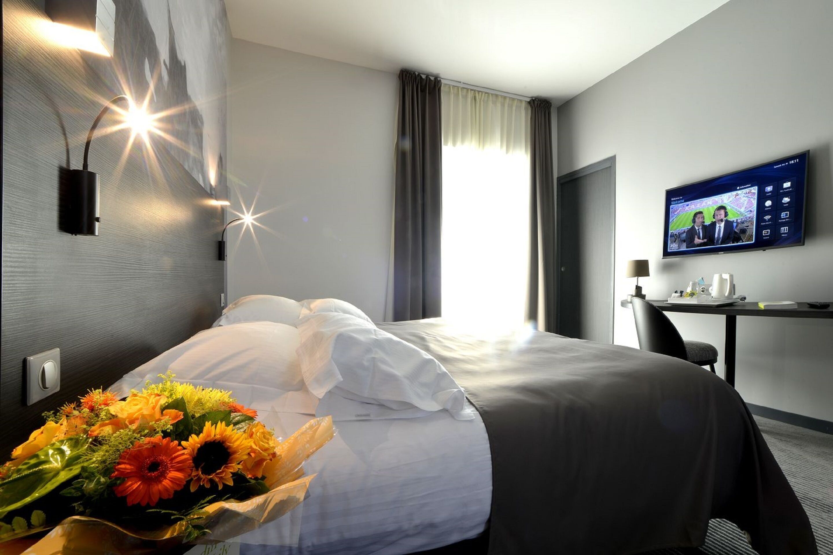 Una habitación de hotel con cama, escritorio, televisor y un ramo de flores.