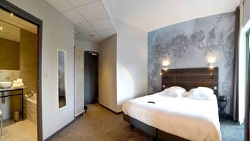 Une chambre d’hôtel avec un grand lit, une salle de bain avec un lavabo et un miroir, et un couloir menant à une autre pièce.