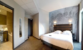 Habitación de hotel con una cama grande, baño con lavamanos y espejo, y un pasillo que conduce a otra habitación.