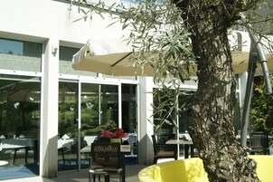 Un área de estar al aire libre con mesas, sillas, un árbol y sombrillas.