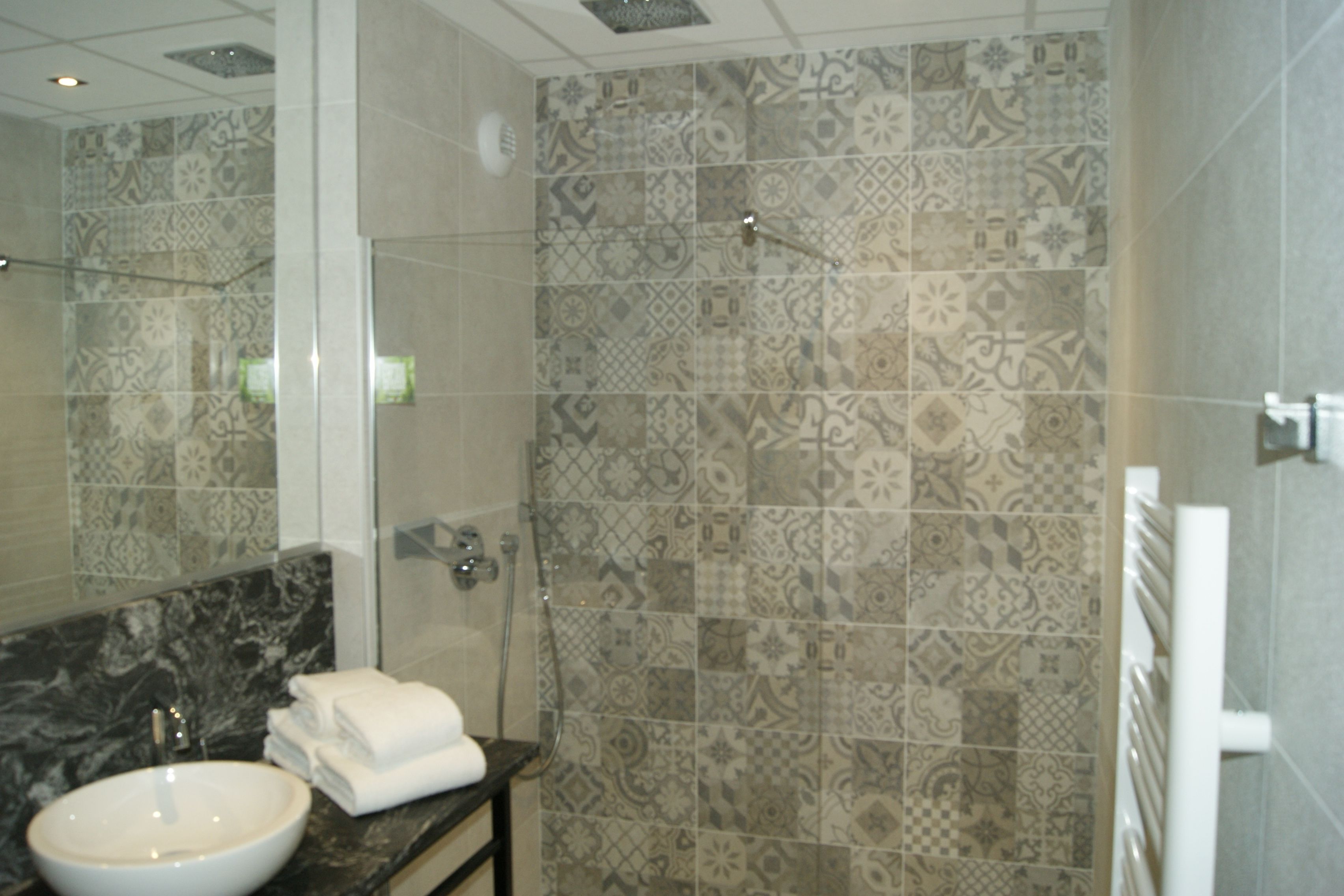 A bathroom with a marble sink, a glass shower enclosure, and patterned tiles.