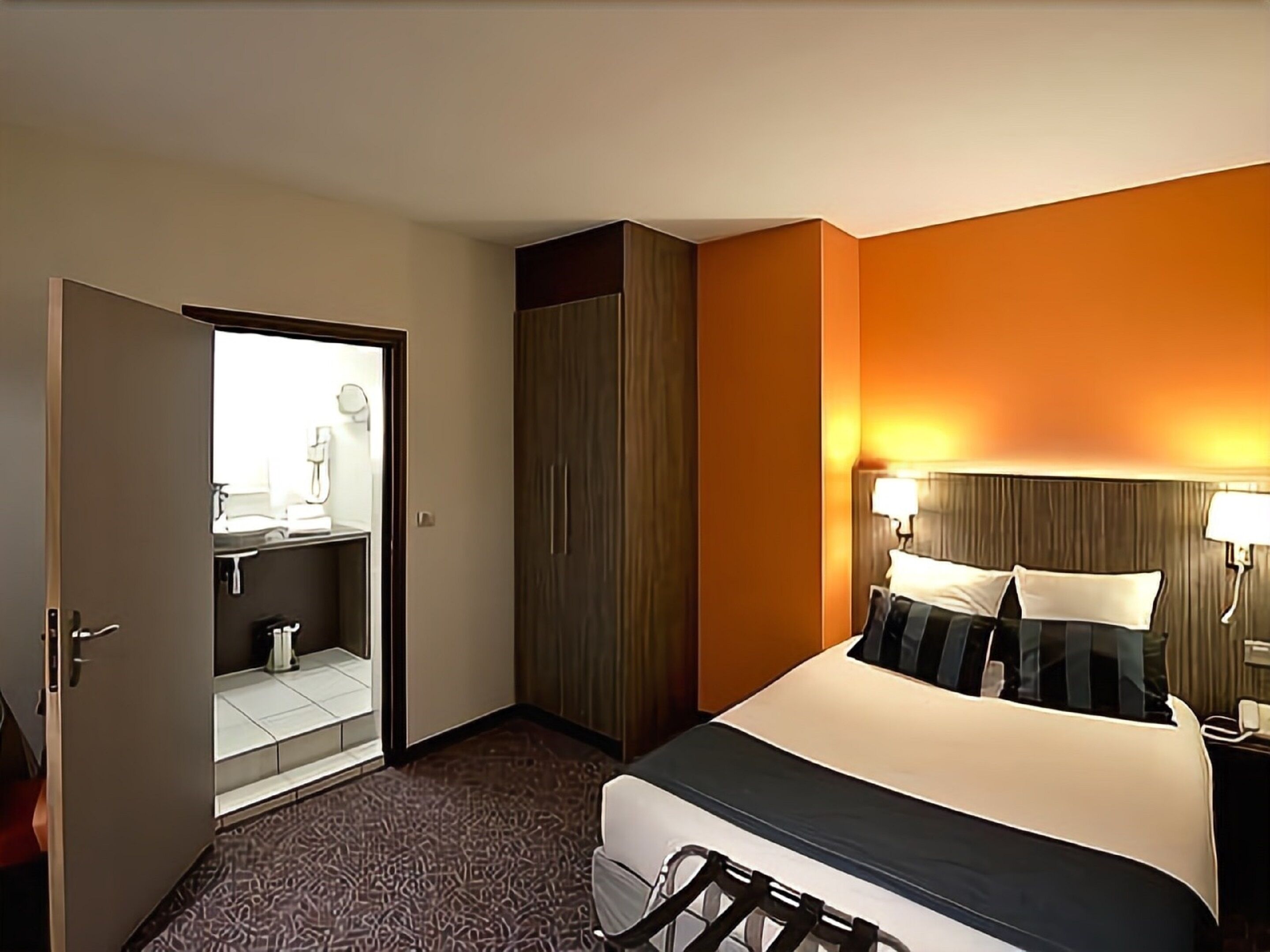 Ein Hotelzimmer mit Bett, Schrank, Badezimmer mit Spiegel und einer Tür zu einem weiteren Raum.