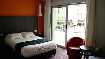 A hotel room with a bed, a red chair, a small table, and a view of the outside balcony.