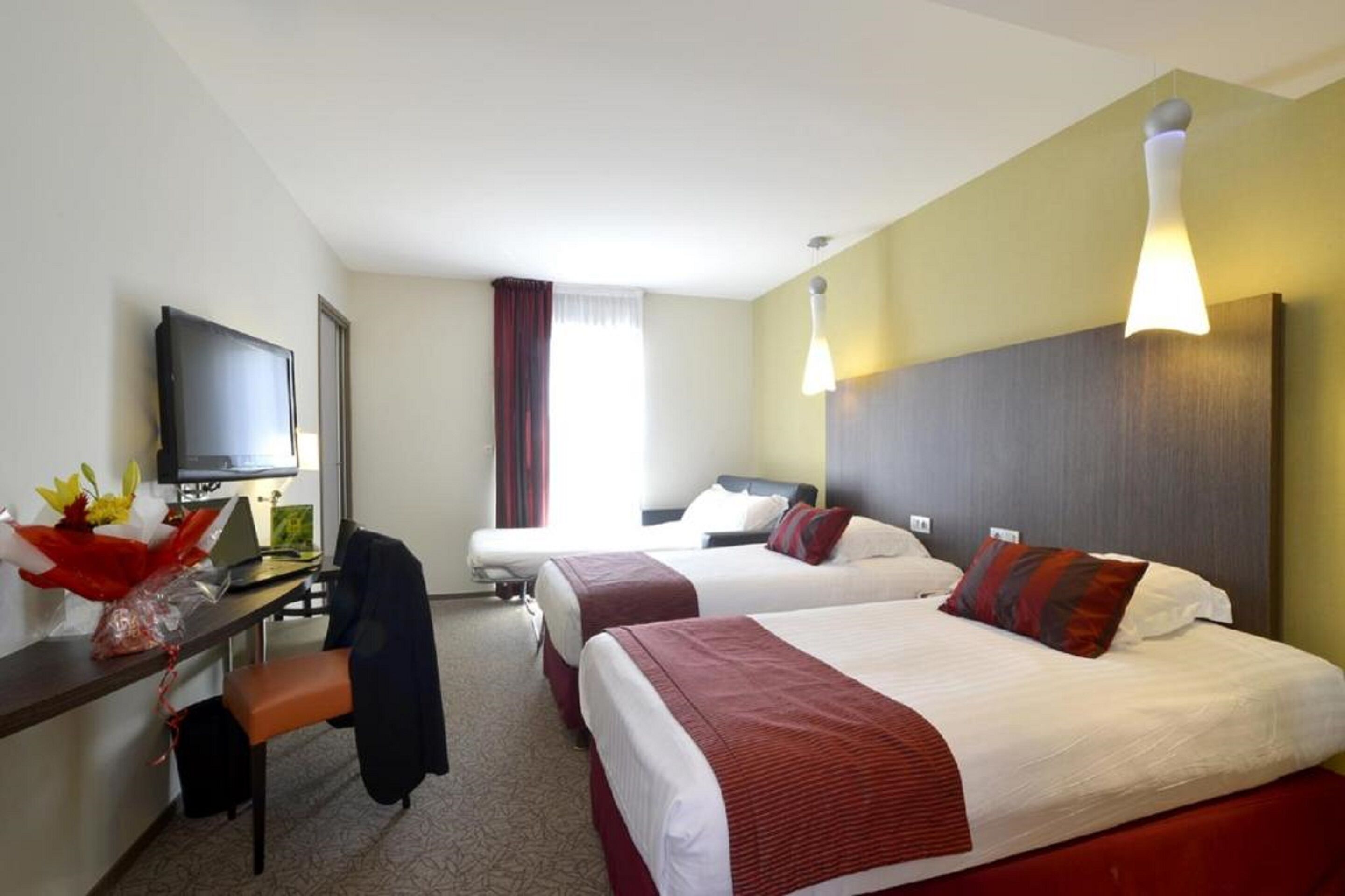 A hotel room with two beds, a desk with a TV, and a chair.