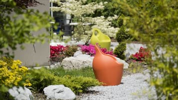 Un jardín con una maceta de terracota grande, una jardinera amarilla y diversas plantas florecientes.