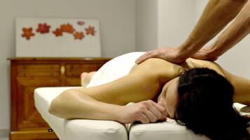 A person receiving a back massage in a room with a wooden cabinet and a framed picture on the wall.