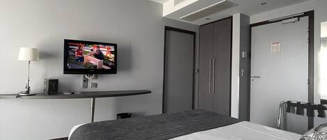Habitación de hotel con cama, televisor en un mueble bajo, escritorio y armario.