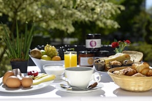 Una mesa de desayuno con huevos, frutas, un vaso de jugo de naranja, una taza de café, pan y pasteles.