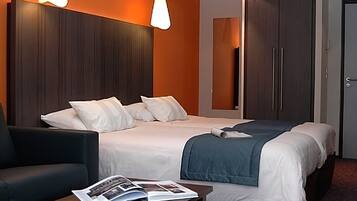 Habitación de hotel con una cama grande, un escritorio con una revista, una silla y un armario.