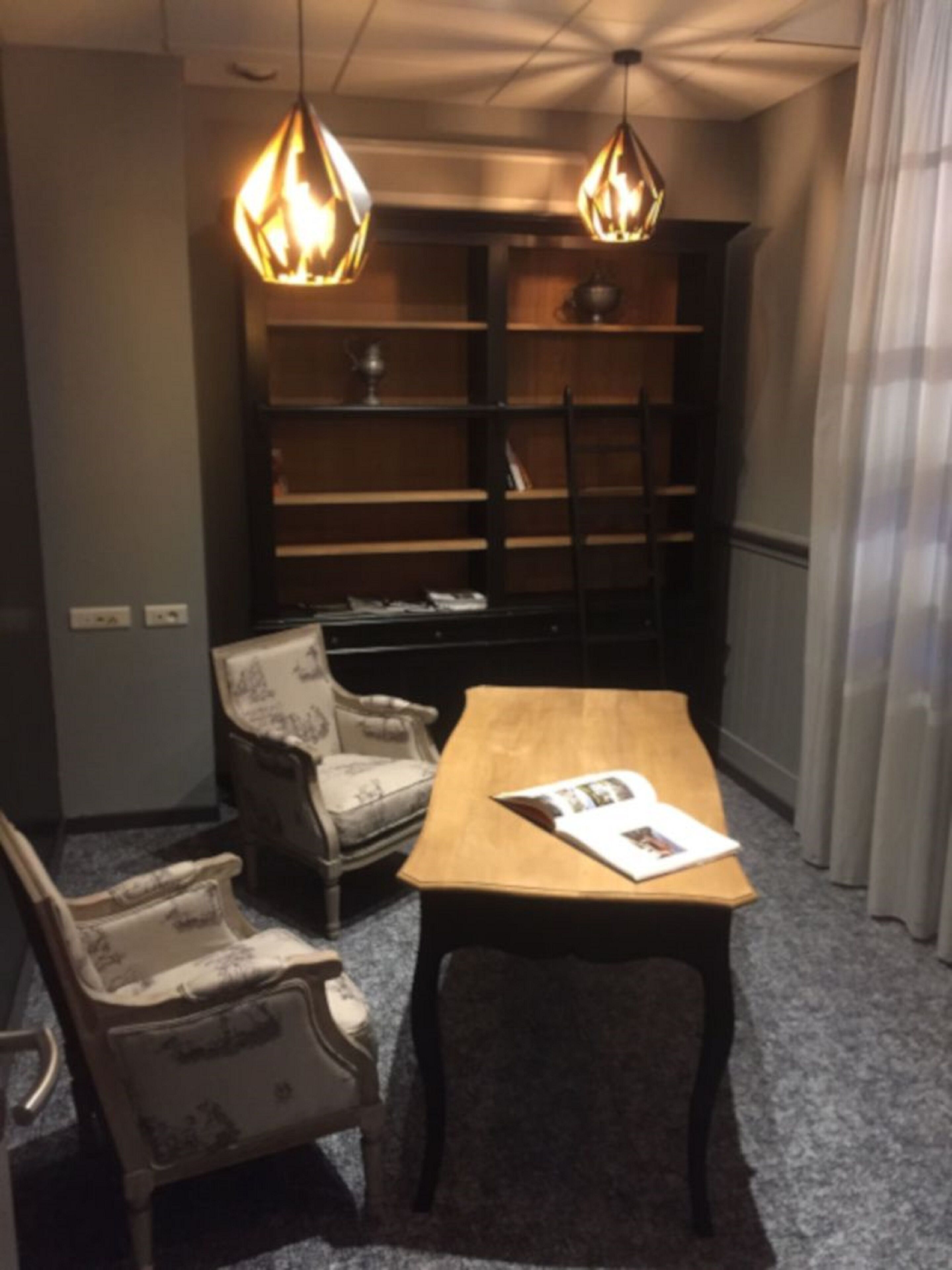A room with a wooden table, two armchairs, a bookshelf, and pendant lights.