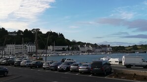 A marina with parked cars and boats, buildings in the background, and a clear sky. - Le Goyen (Audierne)