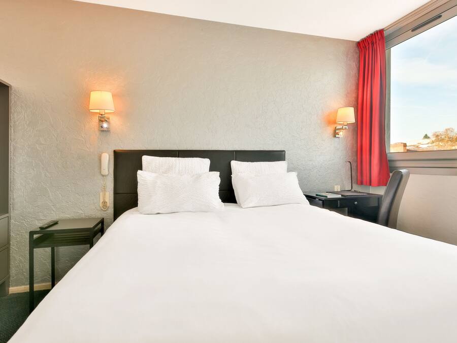 A hotel room with a large bed, two bedside lamps, a desk, and a chair.