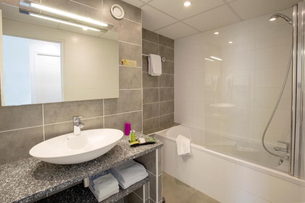 Une salle de bain moderne avec un lavabo blanc, une douche à parois de verre et un miroir au-dessus du lavabo.