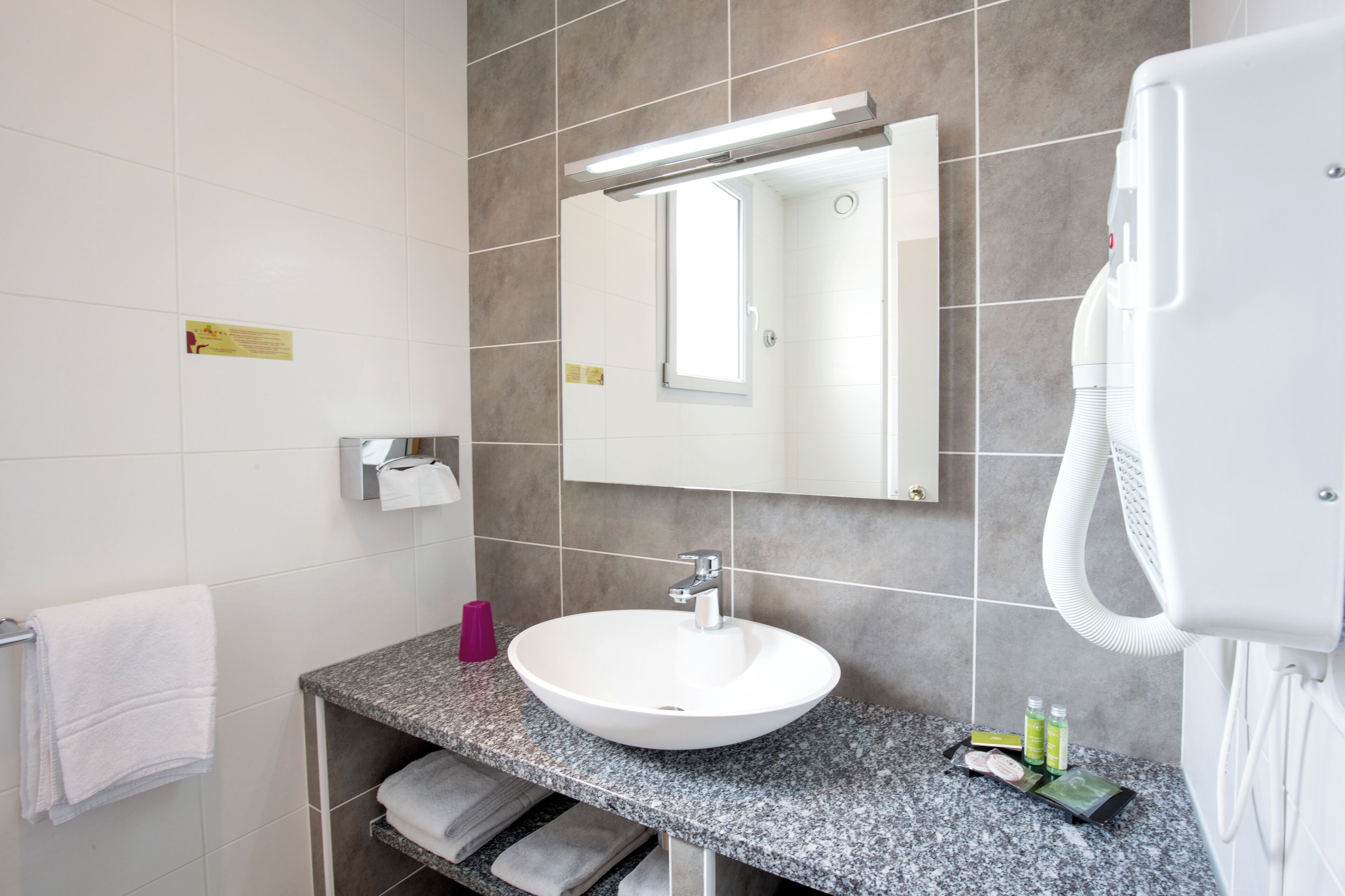 Un baño moderno con un lavamanos blanco, un espejo, un perchero para toallas, un secador de pelo y artículos de aseo en la encimera.