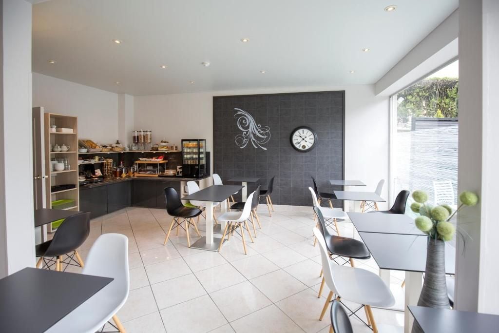 A modern dining area with a kitchen in the background, a clock on the wall, and a large window.