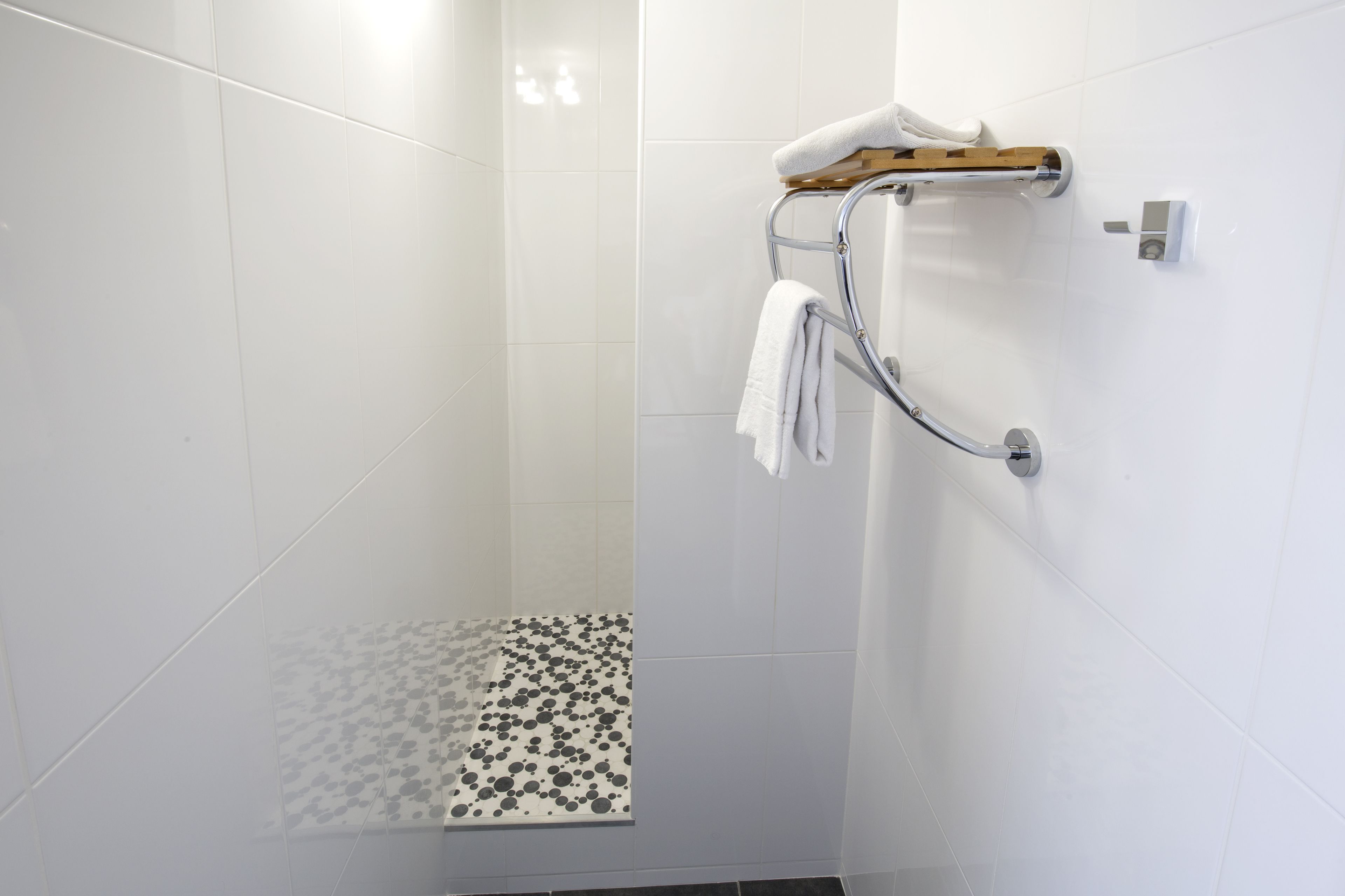 Eine moderne Dusche mit Glastür, weiß gefliester Wand und einem gemusterten Boden.