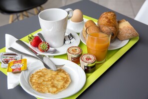 A breakfast tray with pancakes, eggs, croissants, orange juice, jam, and a coffee cup.