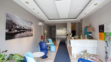 A hotel lobby with a reception desk, seating area, and a corridor leading to the elevator.