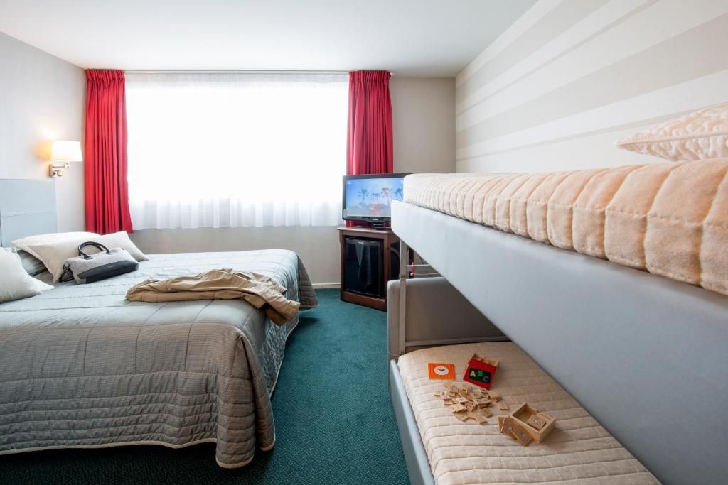 A hotel room with two beds, a television, and a window with curtains.