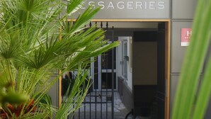 Entrada de un hotel con un letrero que dice "HÔTELES DE BASSAGERIES" y una planta de palmera al frente.