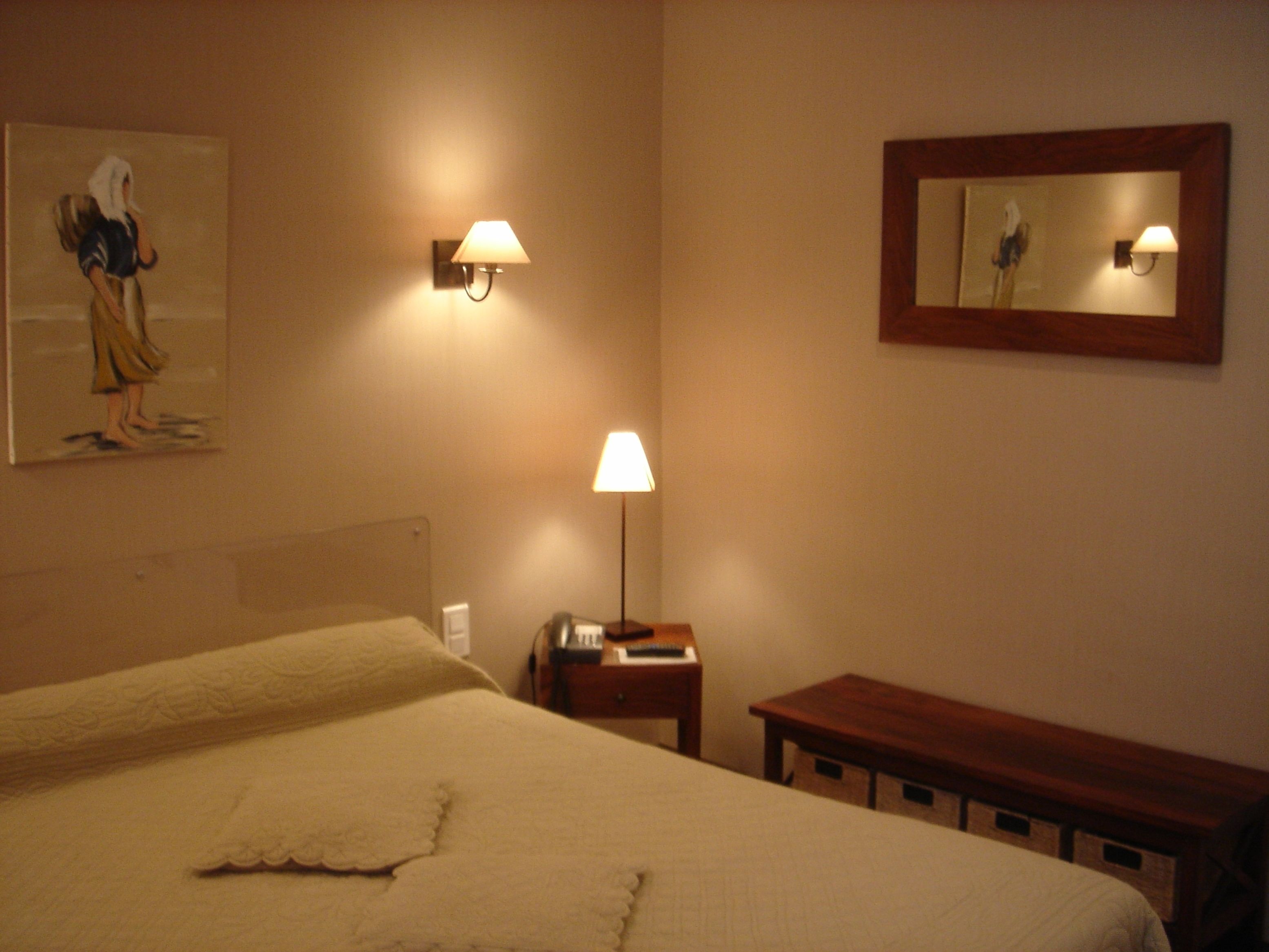 Ein Hotelzimmer mit einem großen Bett, einem Nachttisch, einer Lampe, einem Bild an der Wand und einem Spiegel über dem Bett.
