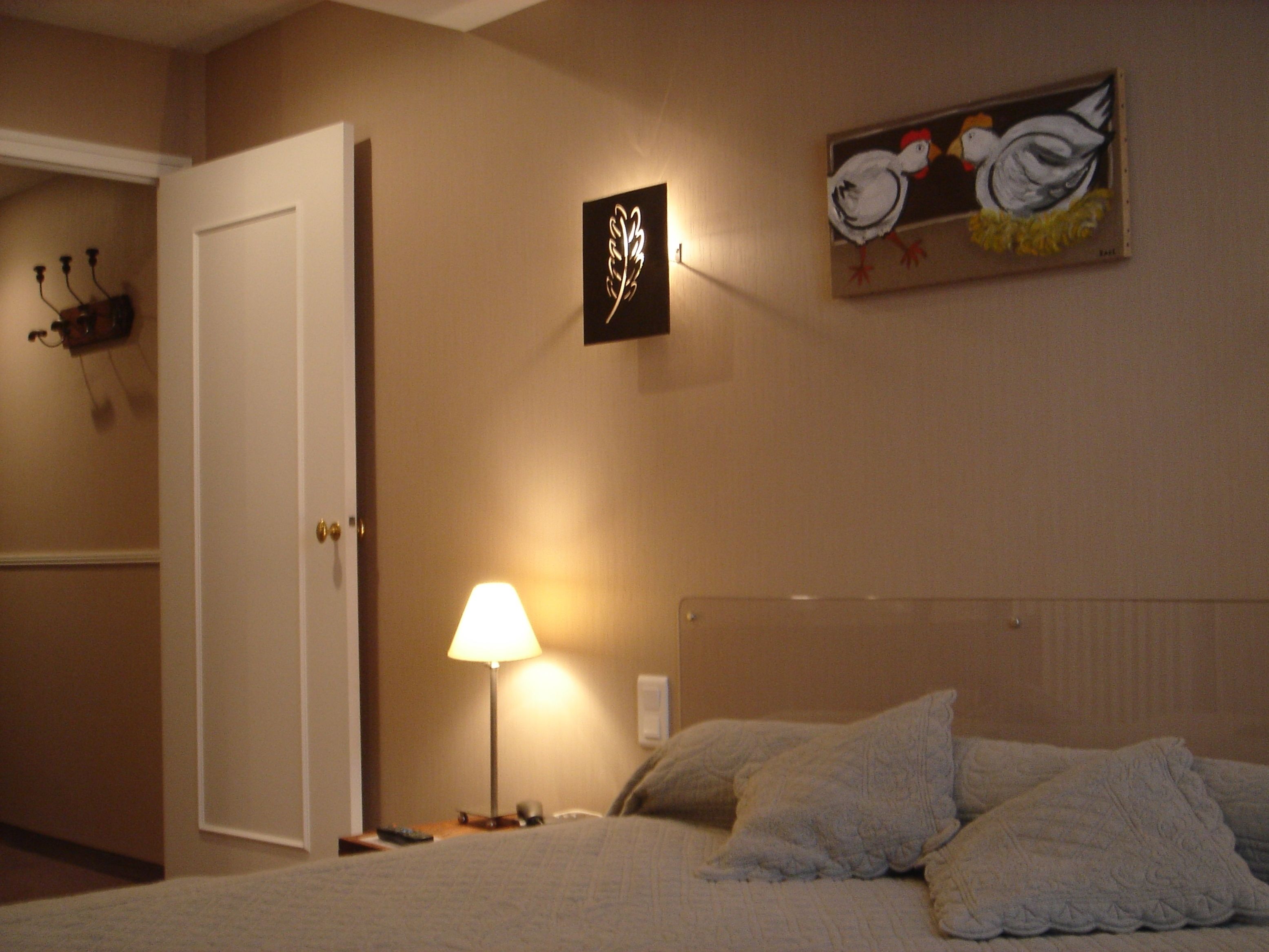 Une chambre d’hôtel avec un lit, une lampe de chevet, un tableau représentant des oiseaux et une porte.