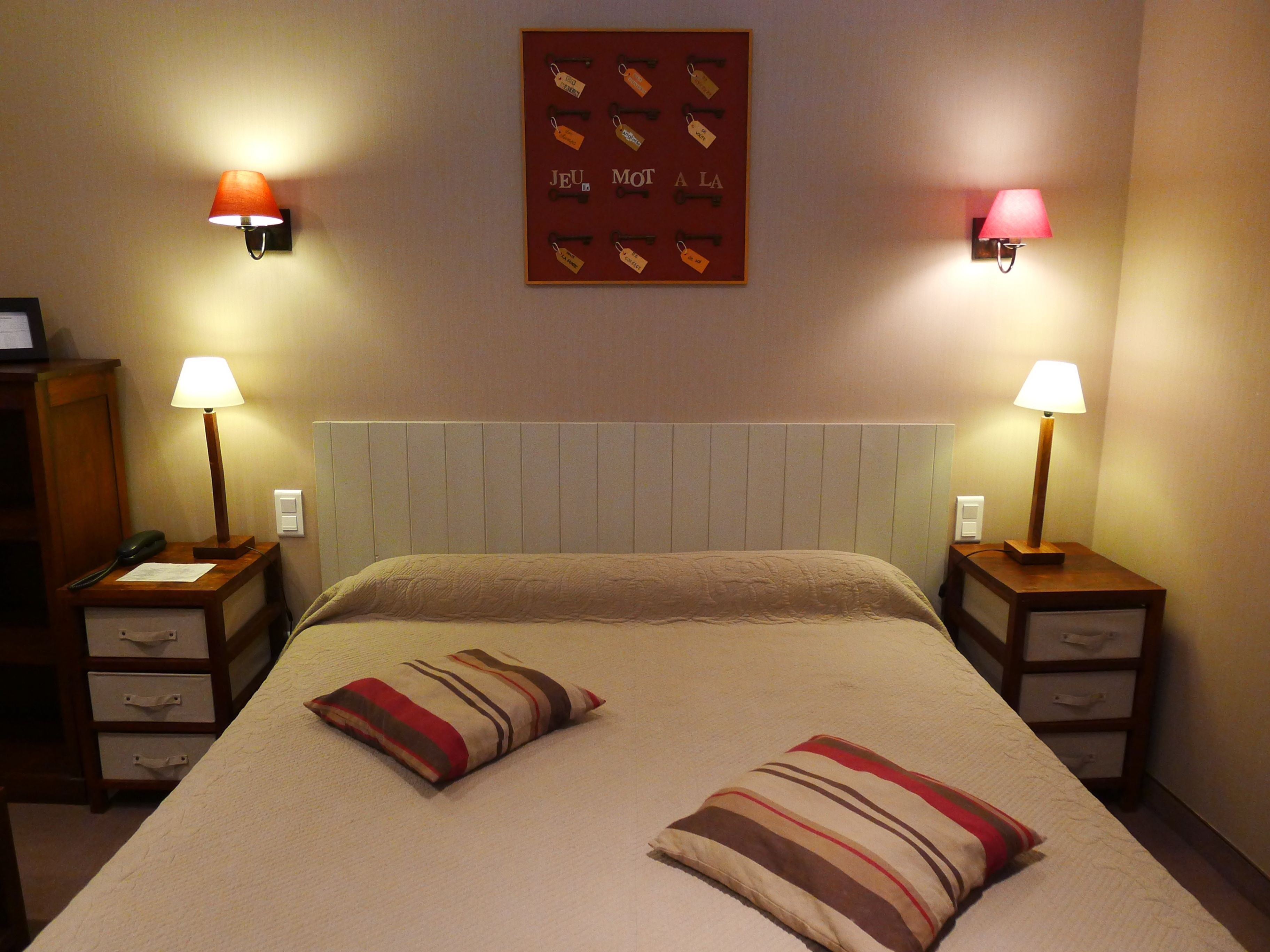 Ein Hotelzimmer mit Bett, zwei Nachttischen, zwei Lampen, einer Wanduhr und einem gerahmten Kunstwerk über dem Bett.