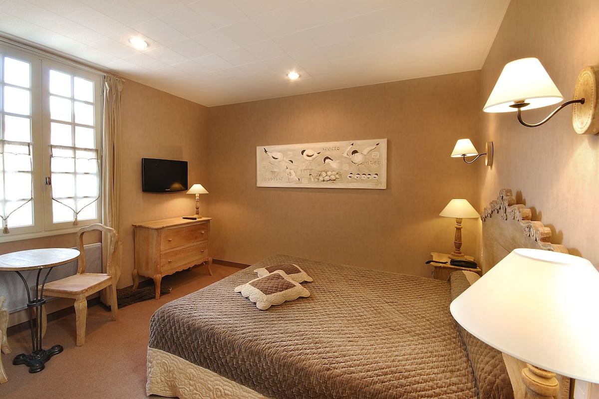 A hotel room with a bed, a desk, a chair, a television, and wall-mounted lamps.