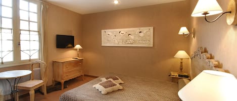 A hotel room with a bed, a desk, a chair, a television, and wall-mounted lamps.