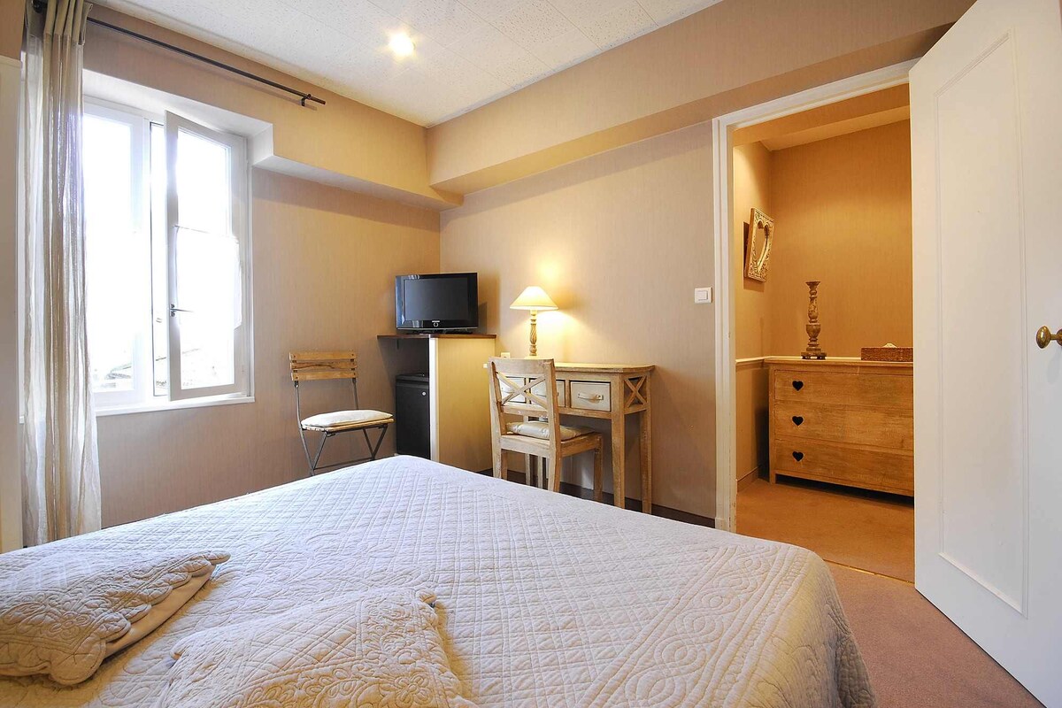 Un dormitorio con una cama, un escritorio con una silla, un televisor, un aparador y una puerta que da a otra habitación.