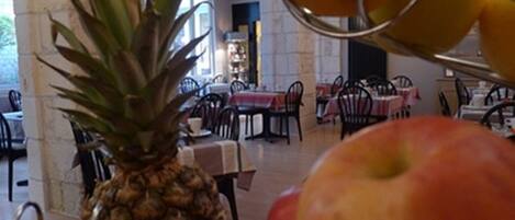 Un comedor con mesas y sillas, una piña sobre una mesa, y un cuenco de fruta.