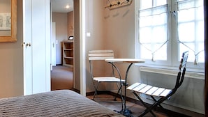 Un dormitorio con una cama, un escritorio y una silla. Se ve una ventana con cortinas y un radiador.