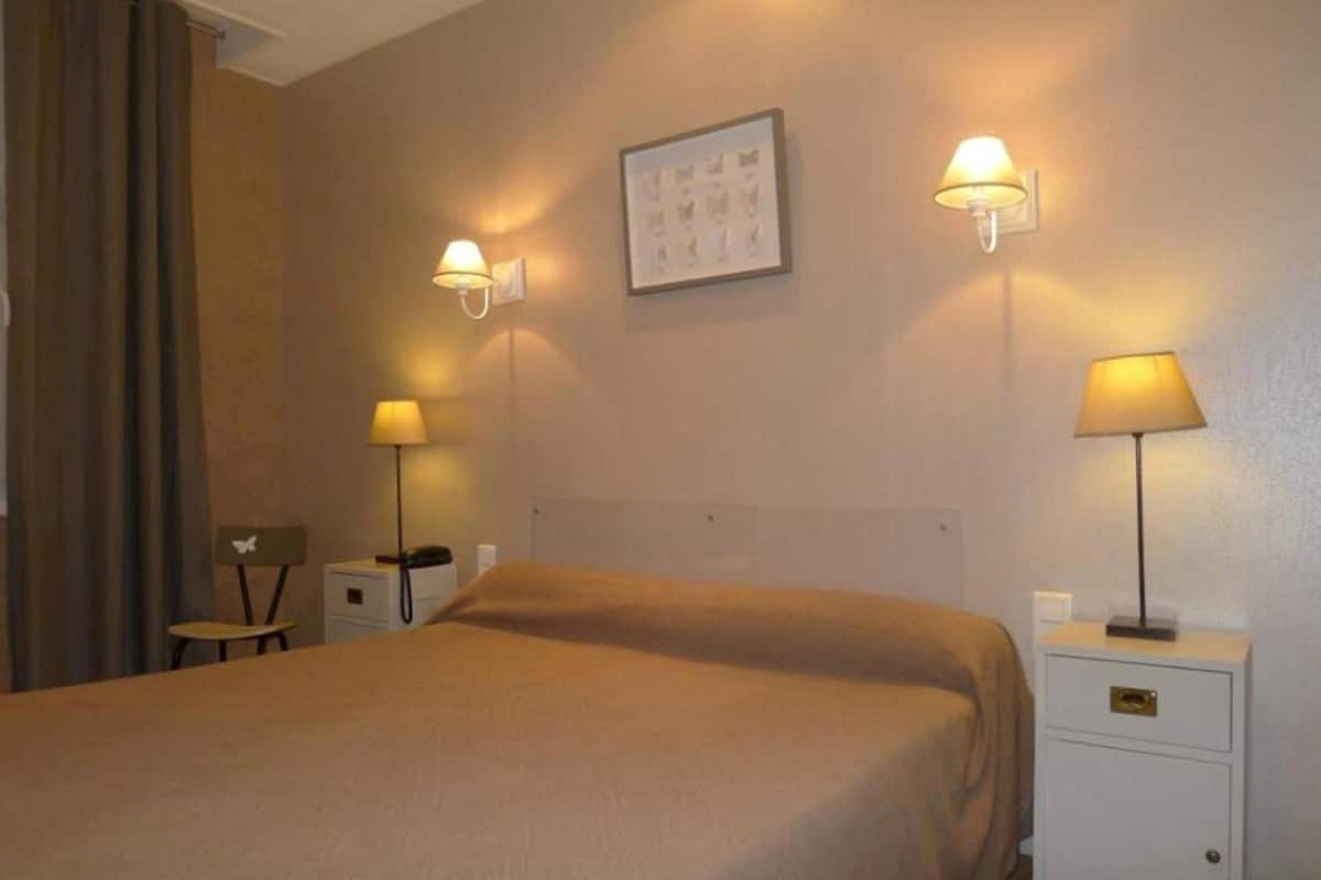 A hotel room with a bed, two bedside tables with lamps, a chair, and a wall-mounted picture.