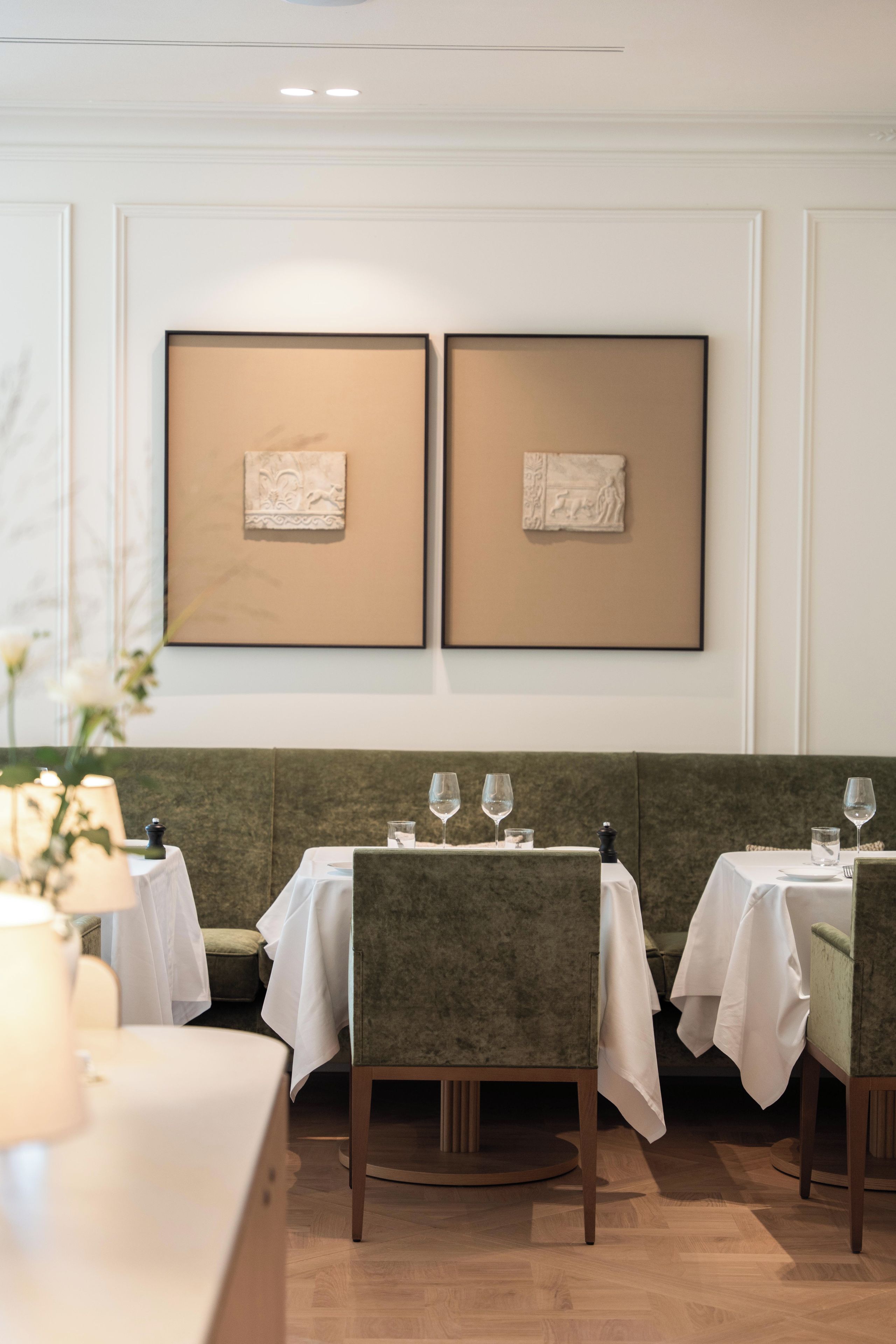 A dining area with two tables, each with four chairs, set against a wall with two framed artworks.