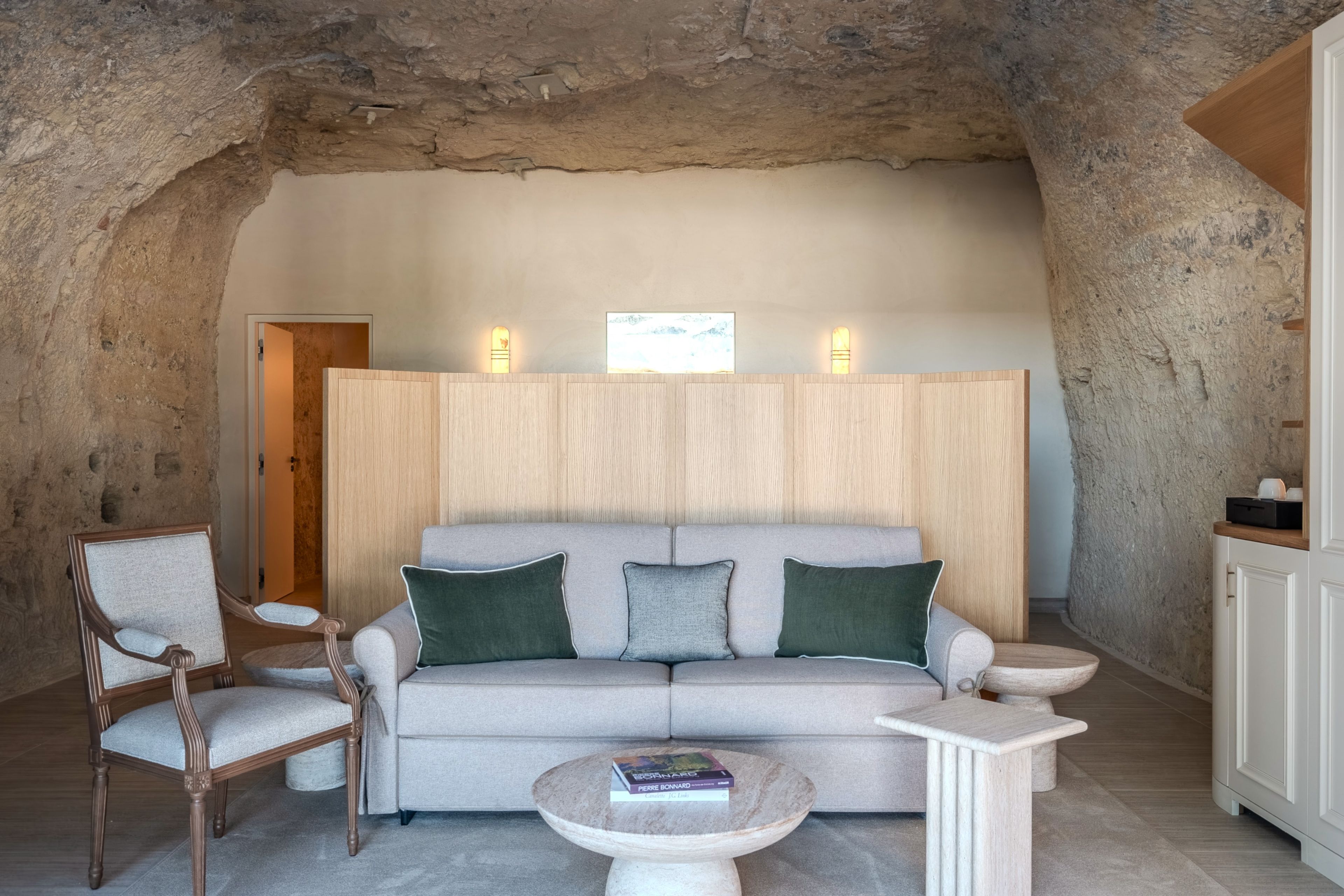 A cozy room with a high ceiling, a sofa with cushions, a wooden chair, a small round table with a book, and a cabinet.