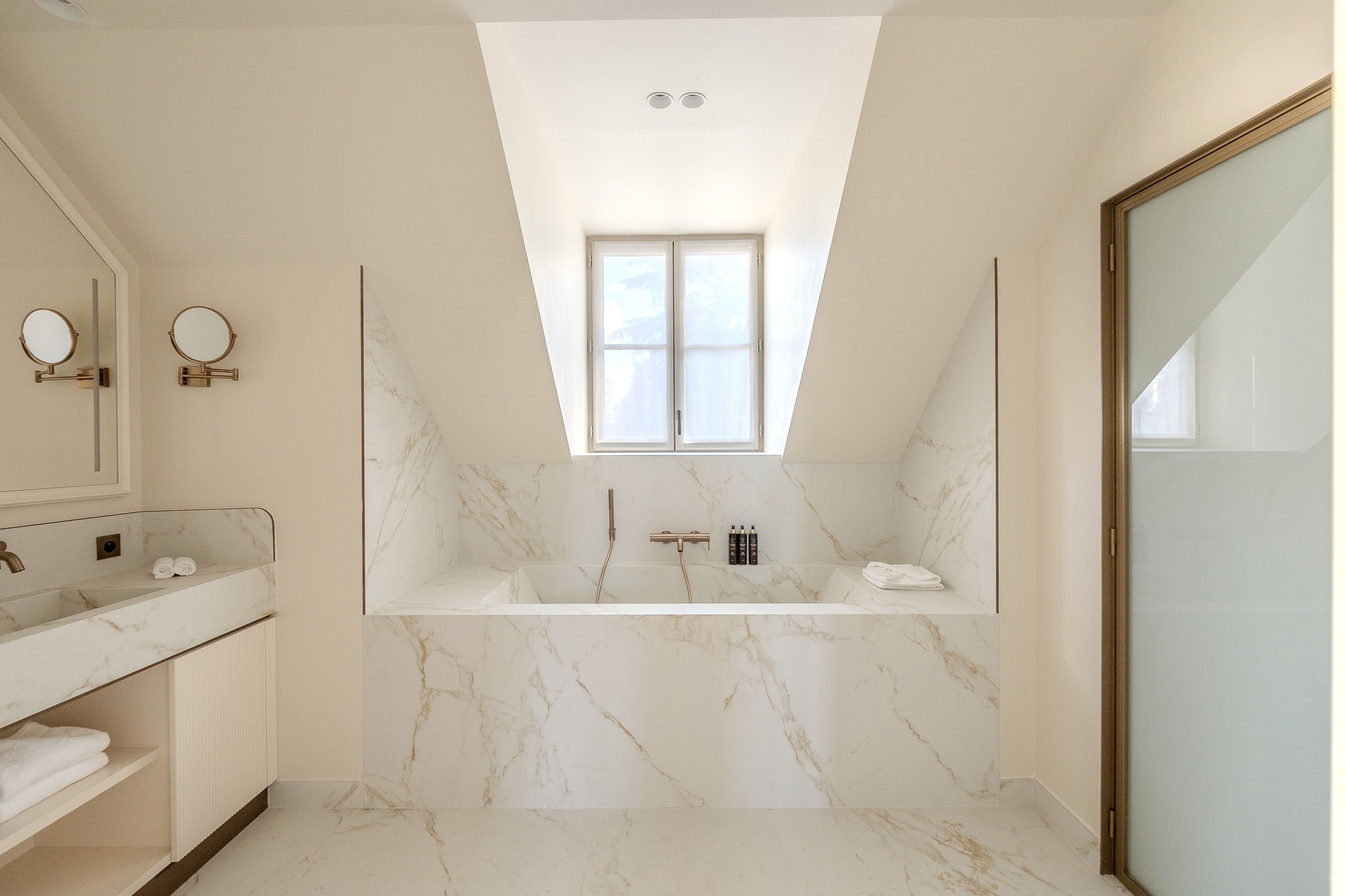 A modern bathroom with a freestanding bathtub, a vanity with a mirror, and a skylight above the shower area.