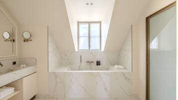 A modern bathroom with a freestanding bathtub, a vanity with a mirror, and a skylight above the shower area.