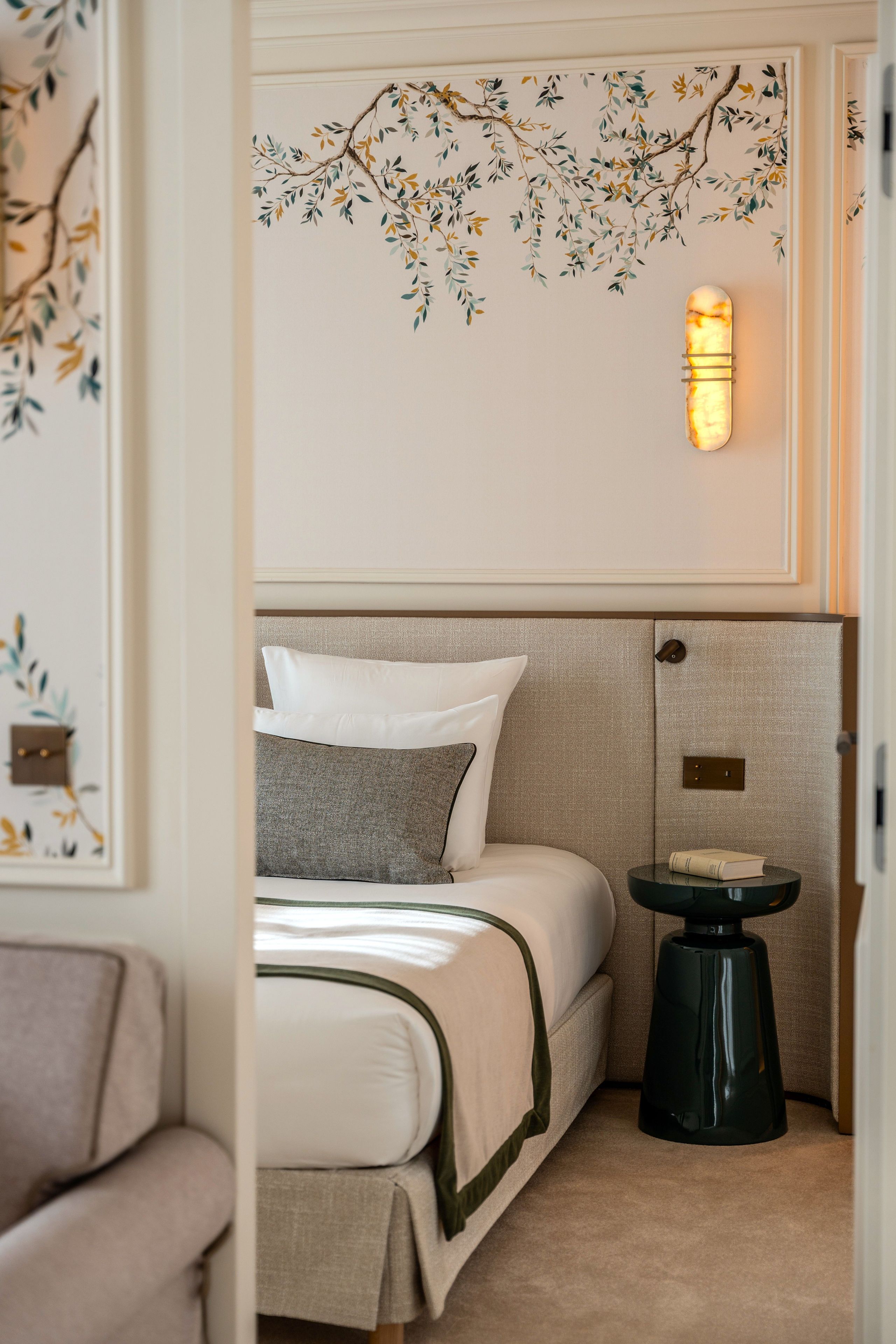 A hotel room with a bed, a bedside table, and a wall-mounted light fixture.
