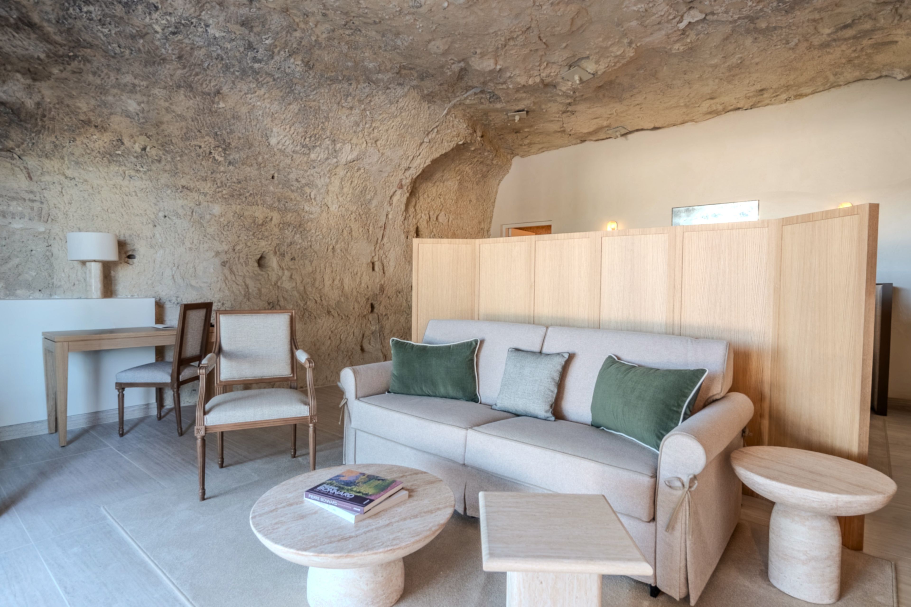 A living room with a stone wall, a sofa, two chairs, a small table, and a lamp.