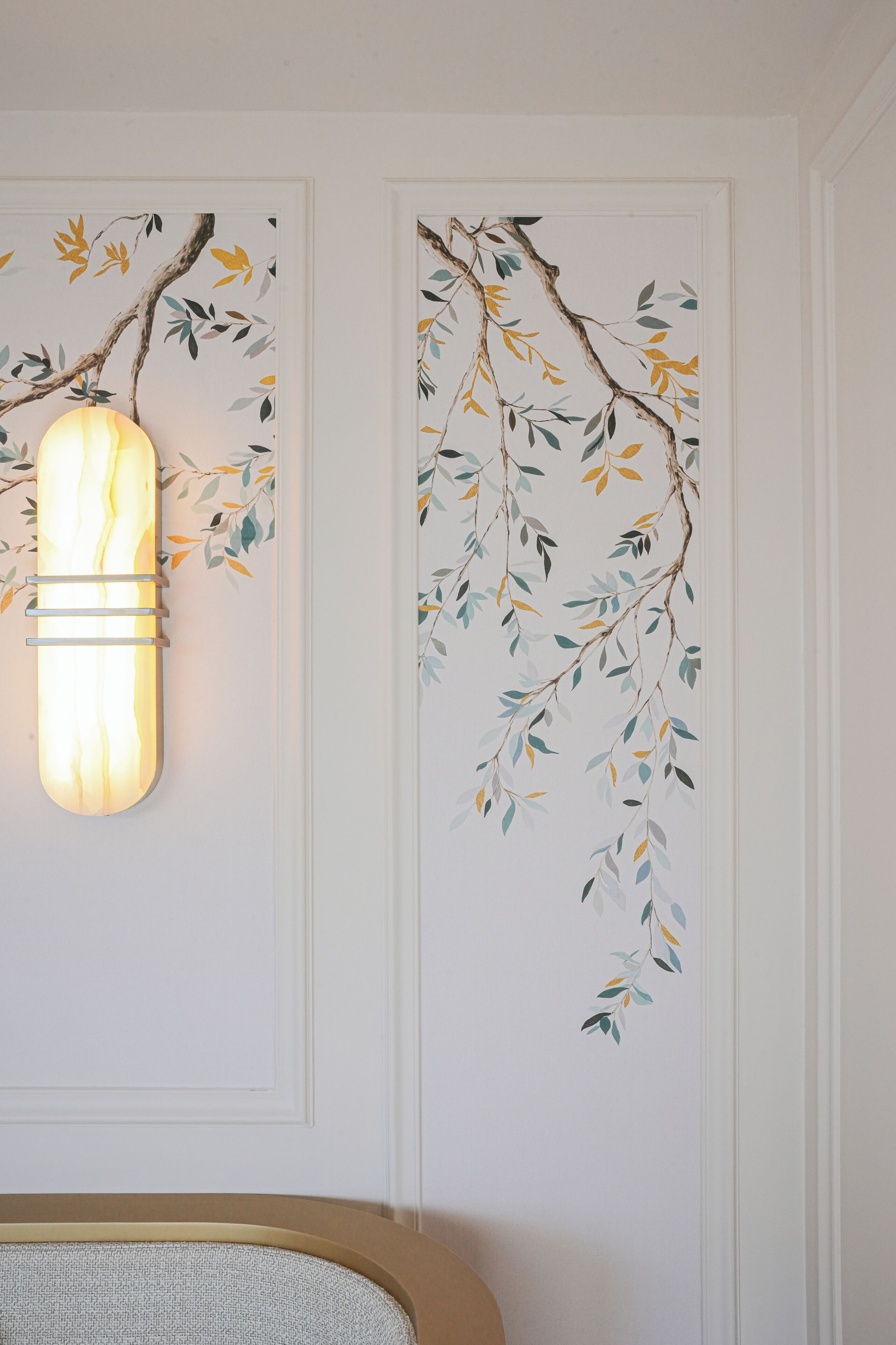 A wall with a branch and leaves design and a wall-mounted light fixture.