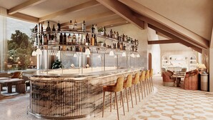 Een bar met een gebogen marmeren toonbank, diverse drankflessen en barstoelen.